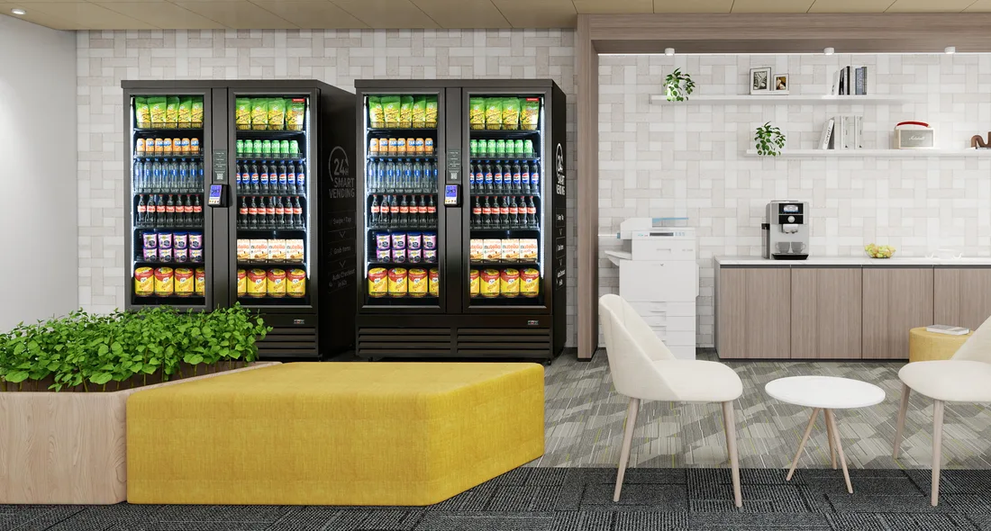 A modern office break room with two dual-door AI Smart Coolers stocked with drinks and snacks, next to a coffee counter and lounge seating